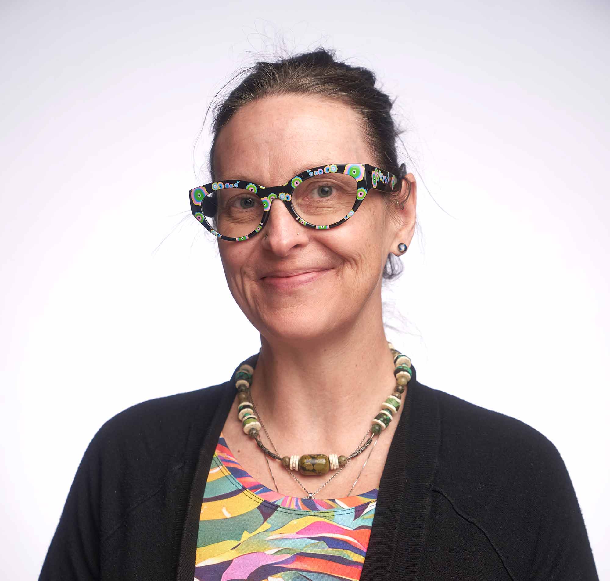BeccaWilliamsHeadshot_Duke headshot portrait of a white woman in her 40s with a colorful patterned shirt and colorful blocky glasses.